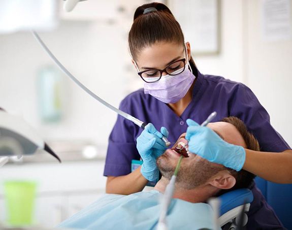 dental hygienist performing cleaning on male patient
