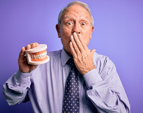A gray-haired man holding a model pair of dentures