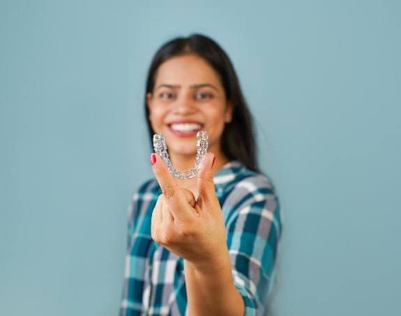 Smiling patient holding up Invisalign clear aligner