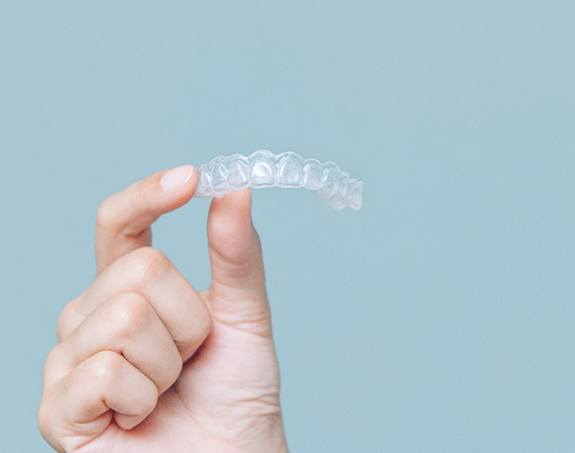 Patient holding clear aligner against light blue background