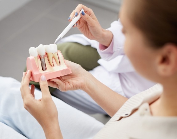 Dentist using model to explain the four step dental implant process