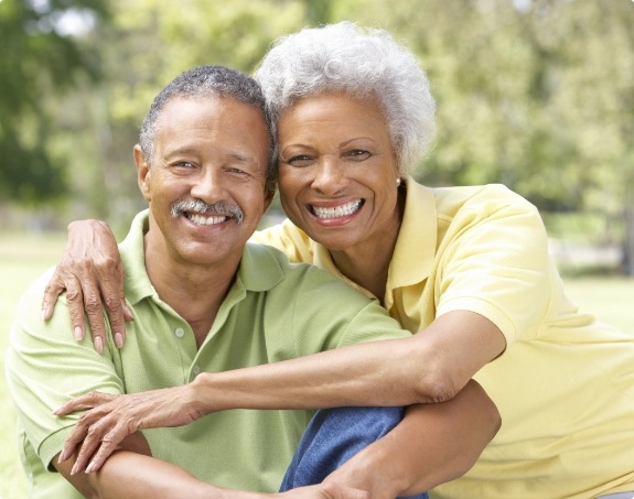 Older couple smiling together after dental implant tooth replacement