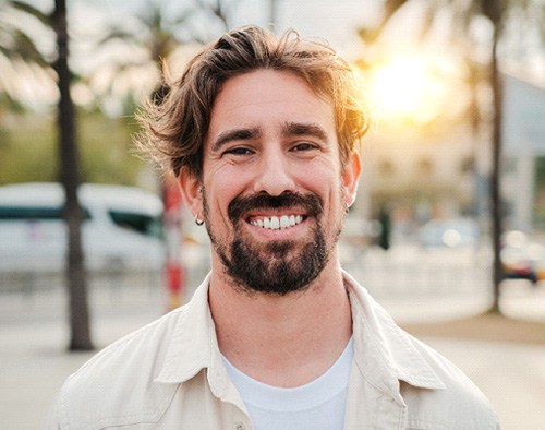 Bearded man walking outside during sunset and smiling