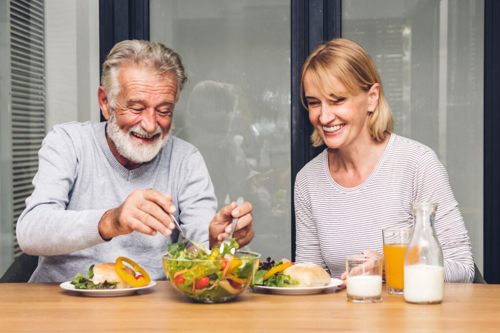 Man with white beard eating salad with woman with blond hair